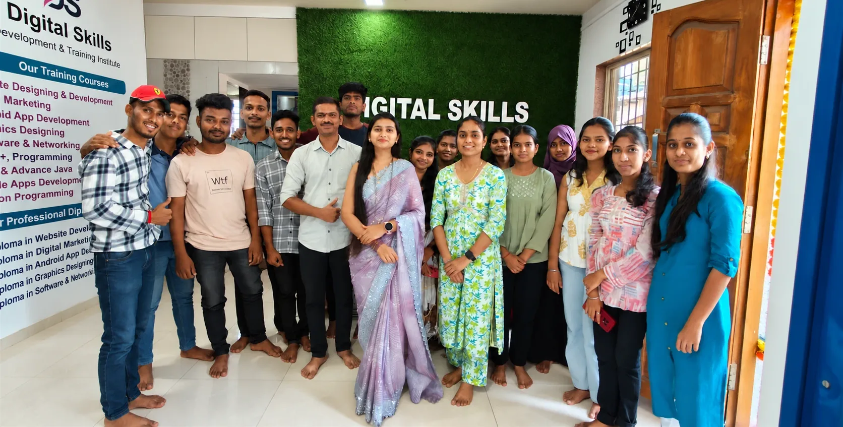 Digital Skills students and trainers in front of the green brand wall in Alibag